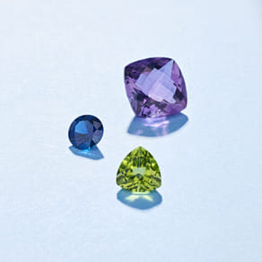 Three colorful gemstones in blue, purple, and green on a light blue background.